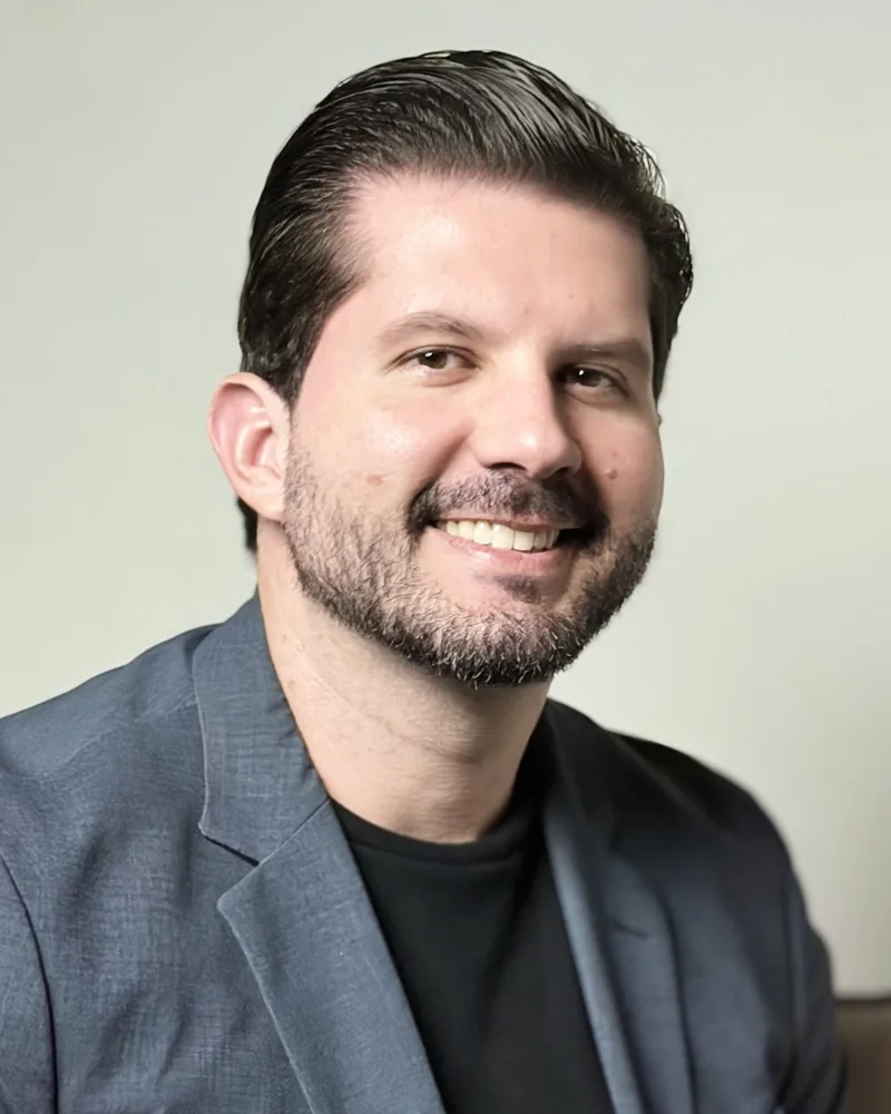 Dr. Joaquim Menezes sentado numa poltrona, de blazer cinza, sorrindo