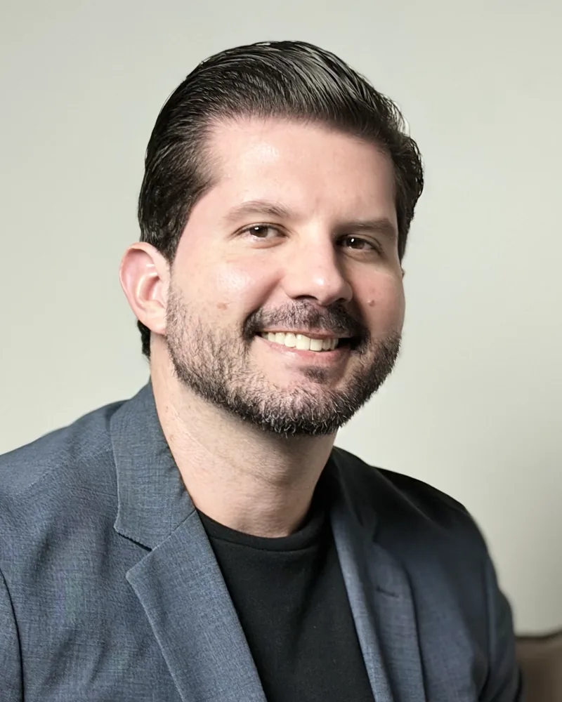 Dr. Joaquim Menezes, de blazer cinza, sorrindo, em estúdio de fundo claro